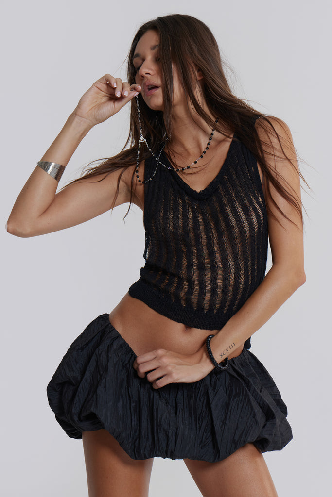 Female model wearing a black balloon style taffeta mini skirt with a puffball hem. Styled with a black knitted top. 