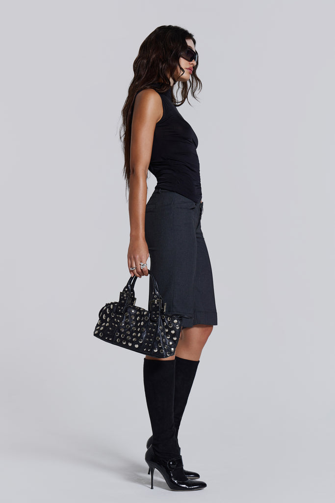 Female model wearing a black high neck top with a twisted back, asymmetric hemline detail and pleated side seam. Paired with charcoal grey tailored shorts. 