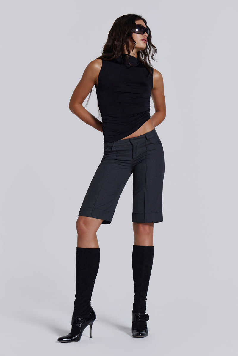 Female model wearing a black high neck top with a twisted back, asymmetric hemline detail and pleated side seam. Paired with charcoal grey tailored shorts. 