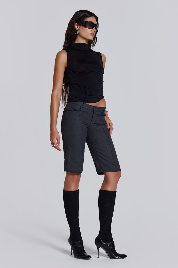 Female model wearing a black high neck top with a twisted back, asymmetric hemline detail and pleated side seam. Paired with charcoal grey tailored shorts. 